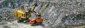 Huge excavator, truck and man standing next on granite quarry. Yellow carver machine, excavator, stonecutter for industrial granite stands in a quarry near granite stones