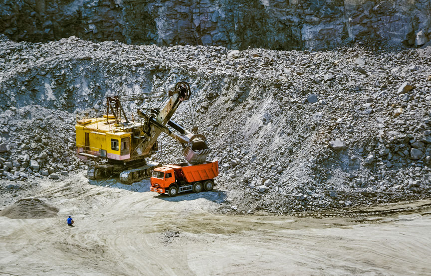 Huge excavator, truck and man standing next on granite quarry. Yellow carver machine, excavator, stonecutter for industrial granite stands in a quarry near granite stones